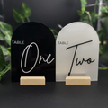 Two table number signs, one black and one white, with wooden stands on a dark background.